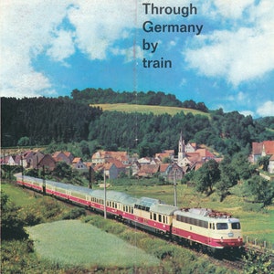 Puede incluir: Un tren de pasajeros rojo y blanco viaja por una campiña rural alemana. El tren viaja por un valle con árboles verdes y casas. El texto "Through Germany by train" está impreso en la parte superior de la imagen.