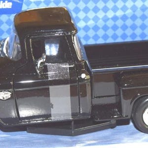 Puede incluir: Modelo de camioneta Chevy Stepside negra de 1955. El modelo tiene un acabado negro brillante, detalles cromados y ruedas detalladas. La camioneta es un vehículo clásico, presentado sobre un fondo azul.