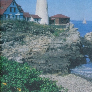 May include: A vintage travel brochure for the state of Maine, featuring a lighthouse on a rocky coastline. The brochure has the text "MAINE" in large yellow letters and "Maine Tourism Association © 2002" in smaller white letters. The brochure also has the text "OFFICIAL HIGHWAY MAP" in blue letters on a yellow background.
