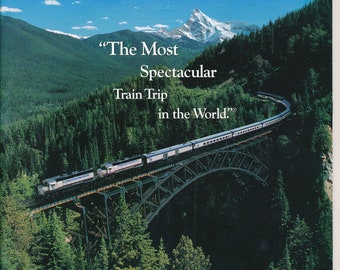 May include: A brochure for a train tour through the Canadian Rockies. The brochure features a photo of a train traveling over a bridge with mountains and trees in the background. The text on the brochure reads "Canadian Rockies by Daylight by Rail" and "The Most Spectacular Train Trip in the World."