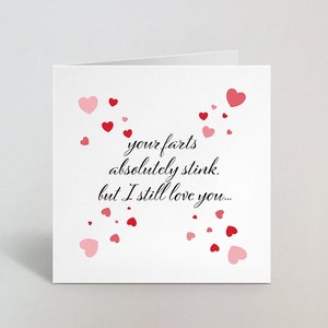 May include: A white greeting card with the text "your farts absolutely stink, but I still love you..." in black script. Red and pink hearts are scattered around the text, creating a romantic and humorous design.