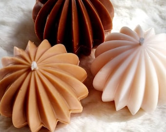 May include: Three decorative candles in the shape of a starburst. The candles are brown, tan, and white.