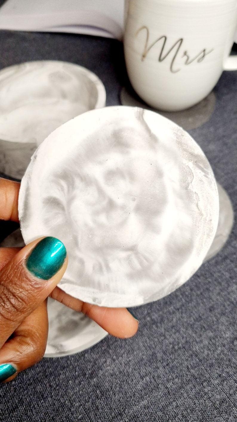 May include: A set of four white and gray marble coasters. The coasters are round and have a swirl pattern.