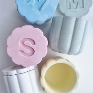 May include: Set of six small decorative containers with scalloped edges. Each container is a different colour and has a letter embossed on the top. The letters spell out the word "SMFTN".