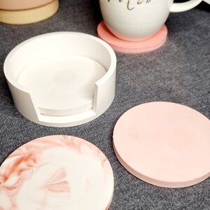 May include: Set of four pink and white coasters. One coaster is a stackable design with a white base and a white top. The other three coasters are solid pink and one has a marbled design with pink and white swirls.
