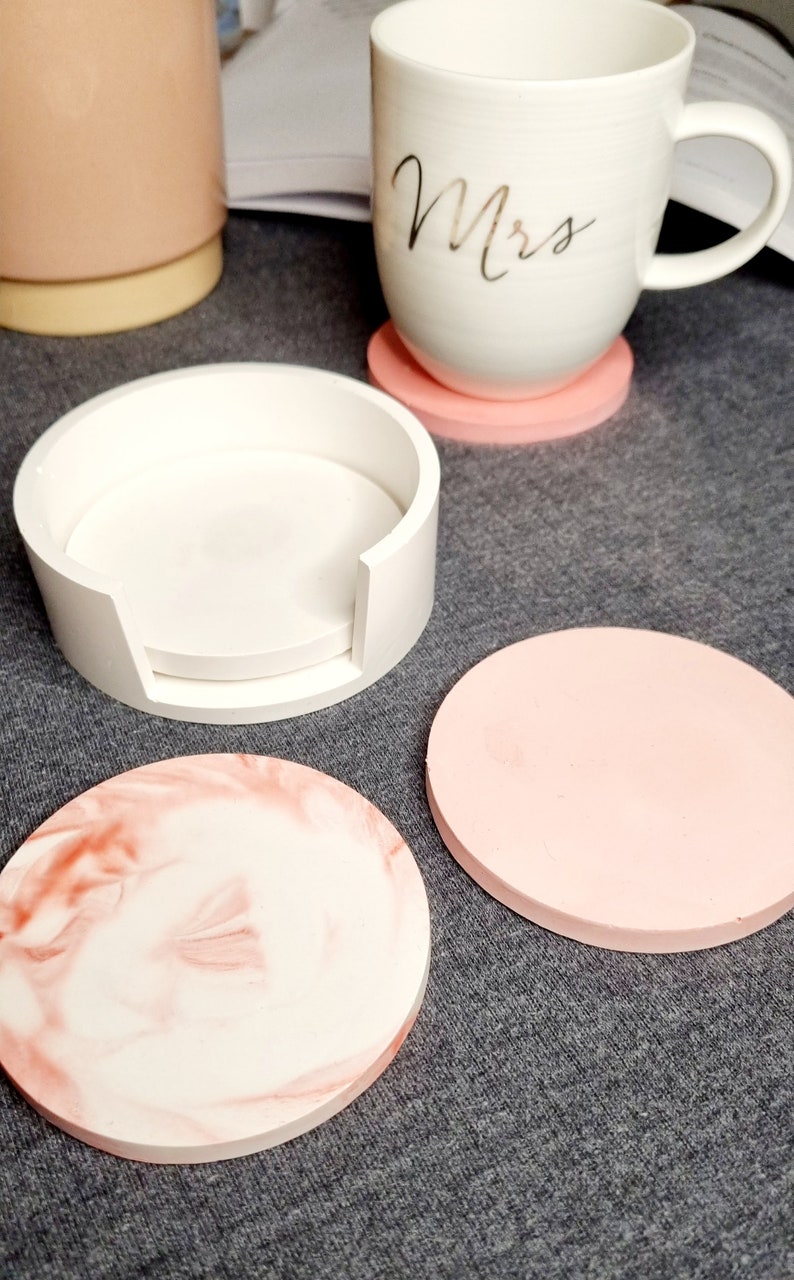 May include: Set of four pink and white coasters. One coaster is a stackable design with a white base and a white top. The other three coasters are solid pink and one has a marbled design with pink and white swirls.