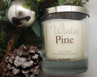 May include: A glass jar candle with a white label that says "Winter Pine" and "A Soy Candle, Handpoured in London. by Linda."