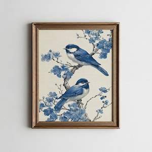 May include: A framed print featuring two blue birds perched on branches with blue flowers. The birds have white markings and are set against a beige background. The frame is gold-colored.