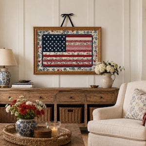 Framed American flag quilt wall art styled in a cozy farmhouse living room with flowers, wood furniture and patriotic decor.