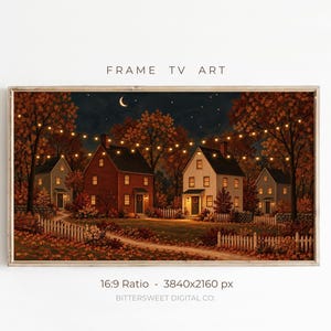 Op de afbeelding: Een digitaal Frame TV-kunstdisplay met een nachtscène van huizen met verlichte ramen, omringd door herfstbomen met oranje bladeren, een wit hekwerk en lichtsnoeren onder een donkere hemel met een maansikkel en sterren.