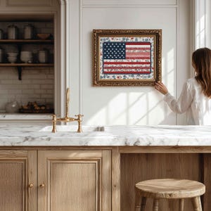 Framed American flag quilt wall art styled in a bright farmhouse kitchen with marble counter, gold faucet and neutral decor.
