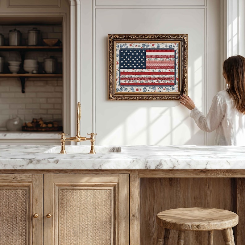 Framed American flag quilt wall art styled in a bright farmhouse kitchen with marble counter, gold faucet and neutral decor.