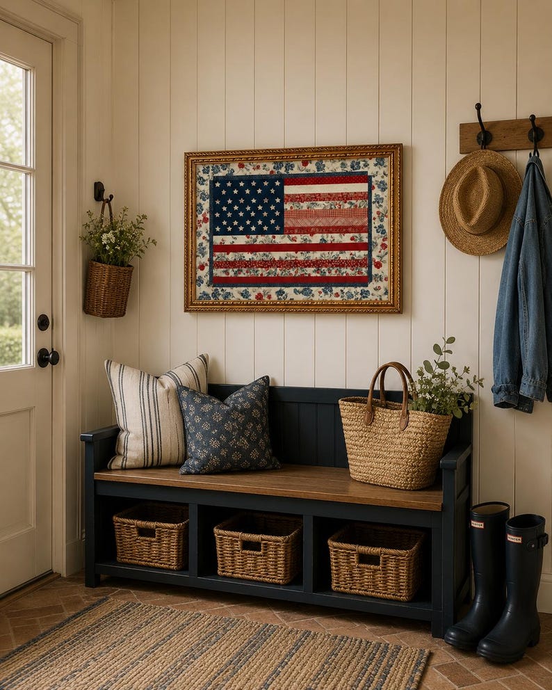 Pode incluir: Uma entrada acolhedora com um edredom emoldurado com a bandeira americana. Um banco azul escuro com tampo de madeira acomoda almofadas, cestos e uma sacola de m&atilde;o tecida. Cestos de vime s&atilde;o guardados embaixo. Um chap&eacute;u de palha e uma jaqueta jeans penduram na parede.