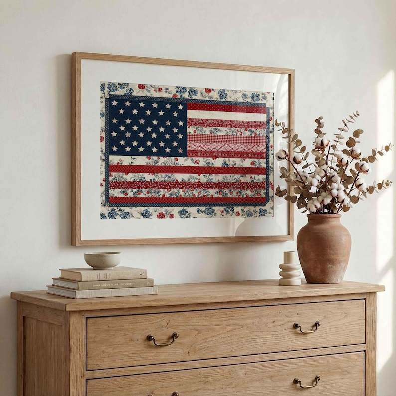 American flag quilt wall art in a light wood frame styled above a wooden dresser with books, vase and neutral farmhouse decor.