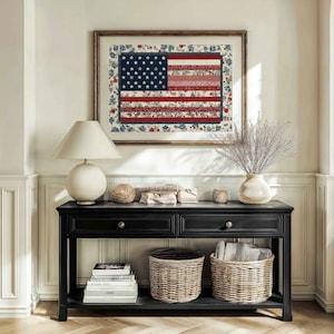 Framed American flag quilt wall art styled above a black console table with baskets, lamp and neutral farmhouse decor.