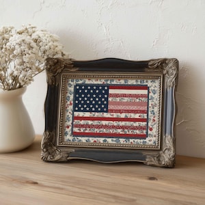 Small framed American flag quilt wall art displayed on a wooden shelf with a white vase and soft neutral farmhouse decor.