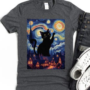 Könnte beinhalten: Dunkelgraues T-Shirt mit einer Illustration einer schwarzen Katze vor einem Sternenhimmel, im Stil von Van Gogh. Die Katze winkt, mit einem skurrilen und künstlerischen Design.