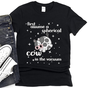 May include: Black t-shirt with a white graphic of a cow in space. The text on the shirt reads "first assume a spherical cow in the vacuum".