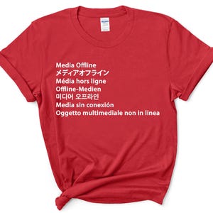 Könnte beinhalten: Rotes T-Shirt mit weißem Text, der in mehreren Sprachen "Medien Offline" lautet, darunter Englisch, Japanisch, Französisch, Deutsch, Koreanisch, Spanisch und Italienisch.