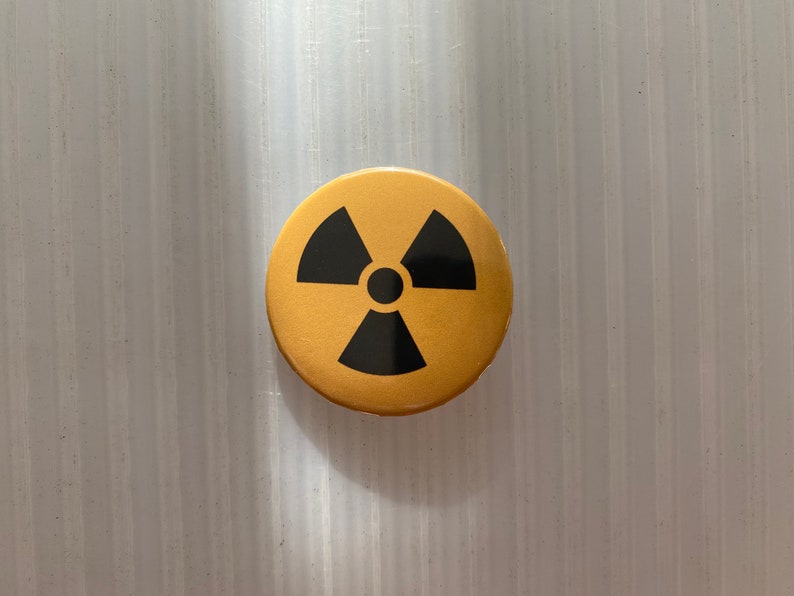 Pu&ograve; includere: Un bottone rotondo dorato con un simbolo di radiazione nero.