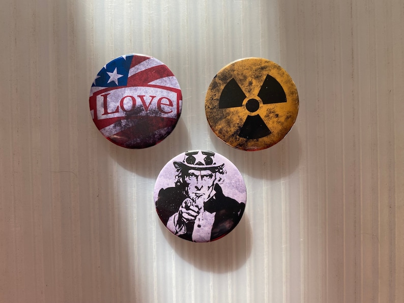 Pu&ograve; includere: Tre spille rotonde con diversi design. La prima spilla presenta una bandiera americana con la parola "Love" stampata su di essa. La seconda spilla presenta un simbolo di radiazione nero e giallo. La terza spilla presenta un'immagine in bianco e nero di zio Sam che punta.