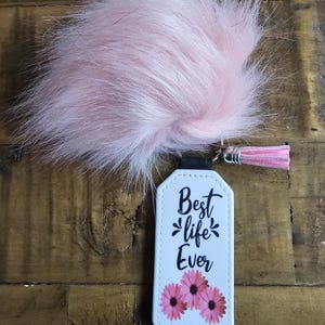 Pode incluir: Chaveiro de couro branco com um pompom rosa peludo. O chaveiro tem o texto "Best life Ever" e tr&ecirc;s flores rosas.