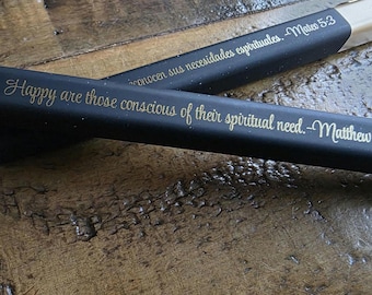 May include: Two black pens with gold lettering. One pen reads "Happy are those conscious of their spiritual need. -Matthew." The other pen reads "conocen sus necesidades espirituales. -Mateo 5:3."