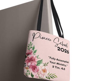 May include: A light pink tote bag with black handles featuring a floral arrangement of pink and white roses with green leaves. The text reads Pioneer School 2026 and Fully Accomplish Your Ministry. 2 Tim. 4:5 in black script and block lettering.
