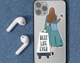 May include: A phone case with a sticker of a woman holding a coffee and a cart that says "BEST LIFE EVER". Two white wireless earbuds are on the left side of the phone. The background is a blue denim texture.