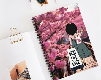 May include: Spiral-bound notebook with a vibrant illustration of a person walking on a bridge under pink cherry blossom trees. The notebook cover features the text "BEST LIFE EVER" on a shopping bag.