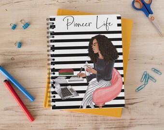 May include: A black and white striped notebook with the text "Pioneer Life" on the cover. The cover also features an illustration of a woman with long curly hair, wearing glasses, a black shirt, and a striped skirt. She is sitting in a pink chair and holding a cup of coffee.