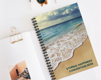 May include: A spiral-bound notebook with a beach scene on the cover. The cover features a photograph of a sandy beach, turquoise water, and a cloudy sky. The text "ETERNAL HAPPINESS CONVENTION 2026" is printed on the cover.