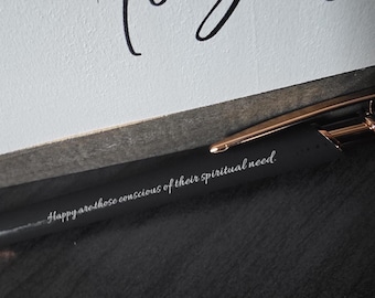 May include: A black pen with gold accents, featuring the inscription "Happy are those conscious of their spiritual need." The pen is positioned near a white surface with the word "Together" in black script.