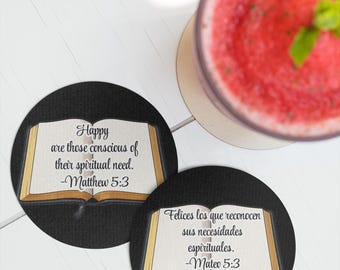 May include: Two black round coasters with a Bible illustration and text from Matthew 5:3. One coaster reads "Happy are those conscious of their spiritual need." A glass of red drink is in the background.