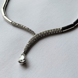 May include: A silver necklace with a pear-shaped pendant set with clear stones. The necklace is made of a series of connected silver bars, each with a row of small clear stones.