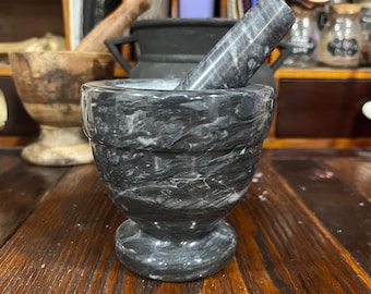 May include: A black and white marble mortar and pestle. The mortar is round and has a wide base. The pestle is long and slender.