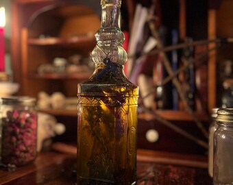 May include: A clear glass bottle with a cork stopper filled with a golden liquid and dried herbs. The bottle is sitting on a wooden surface.
