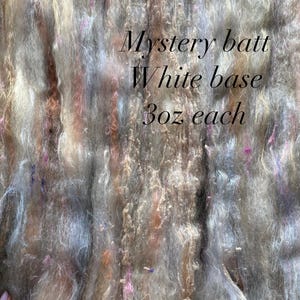 May include: A close-up of a fiber batt with a white base, featuring a blend of gray, brown, and pink fibers. The text "Mystery batt White base 3oz each" is visible. The fiber is soft and fluffy, ideal for spinning or felting.