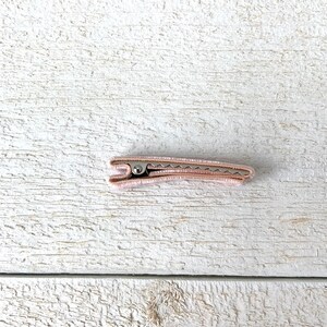 Puede incluir: Una pinza para el pelo de color rosa claro con un resorte met&aacute;lico.