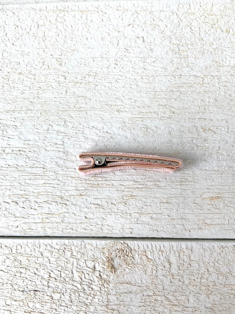 Puede incluir: Una pinza para el pelo de color rosa claro con un resorte met&aacute;lico.