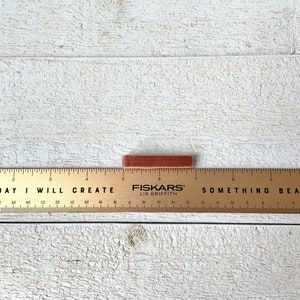 Puede incluir: Un palo de tiza rectangular marr&oacute;n sobre una superficie de madera blanca con una regla que dice "DAY I WILL CREATE" y "FISKARS LIA GRIFFITH" y "SOMETHING BEAUTIFUL".