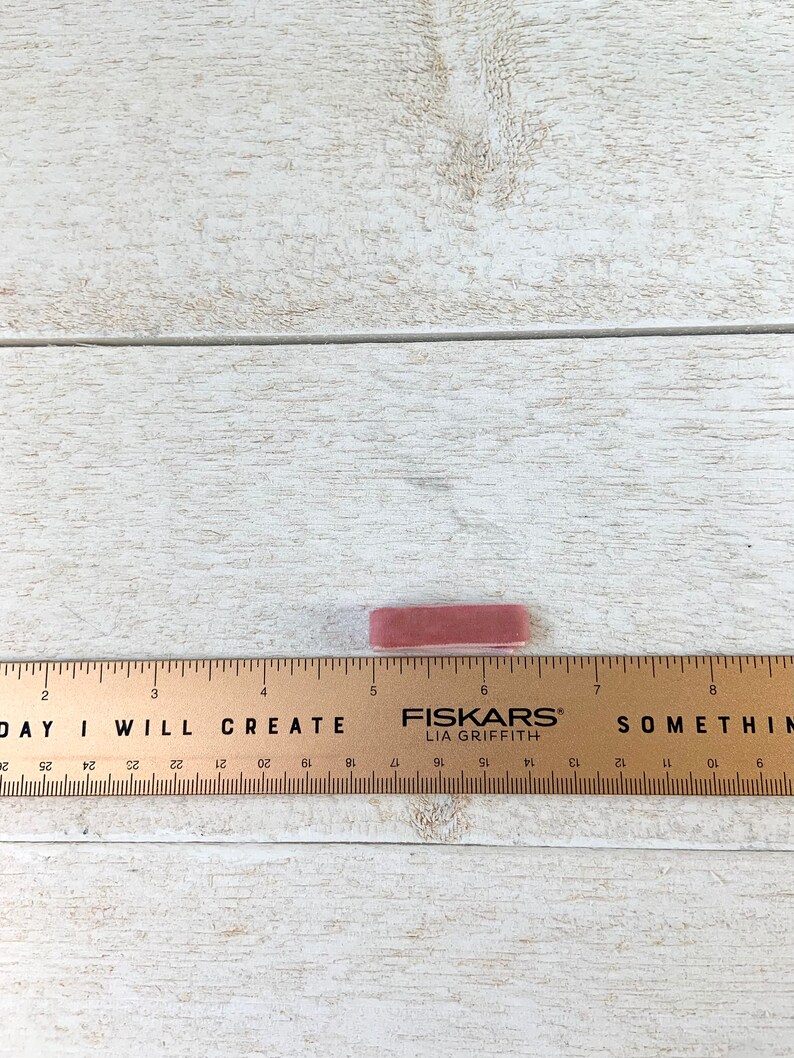 May include: A close-up of a pink eraser with the text "FISKARS&reg; LIA GRIFFITH" printed on it. The eraser is sitting on a wooden surface with a ruler marked with inches.