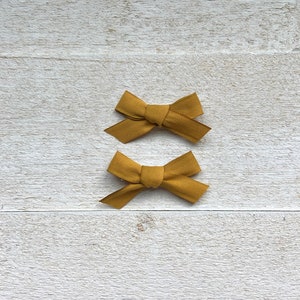 May include: Two mustard yellow fabric hair bows on a white wooden background.