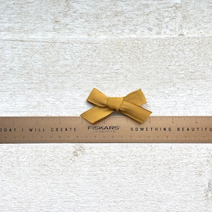 May include: A wooden ruler with the words "TODAY I WILL CREATE SOMETHING BEAUTIFUL" printed on it. A small mustard yellow bow is placed on top of the ruler.