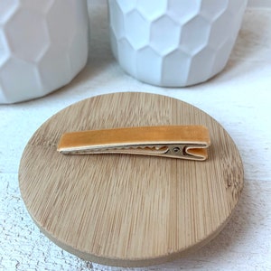 May include: A light brown velvet hair clip with a gold metal clasp. The clip is sitting on a wooden surface.