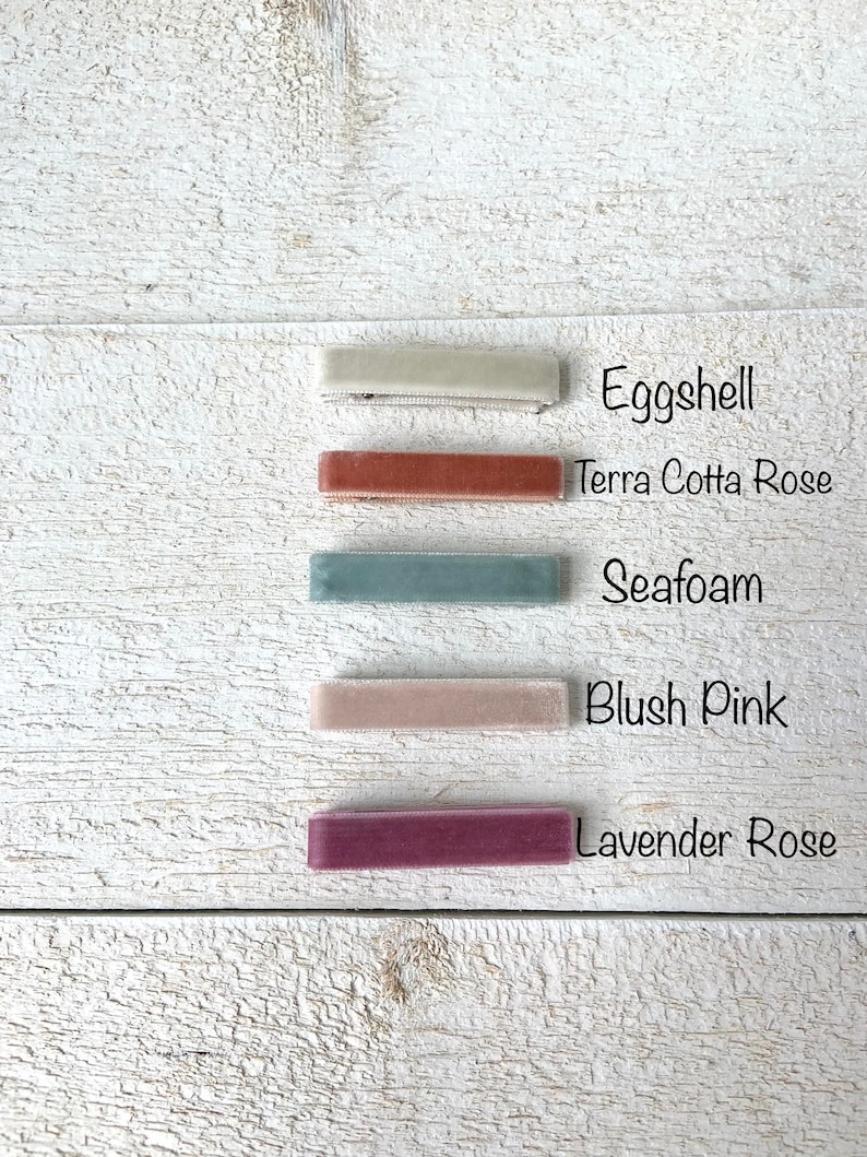 Puede incluir: Cinco pinzas para el pelo de terciopelo en diferentes colores: c&aacute;scara de huevo, rosa terracota, espuma de mar, rosa rubor y rosa lavanda. Las pinzas est&aacute;n dispuestas verticalmente sobre una superficie de madera blanca.
