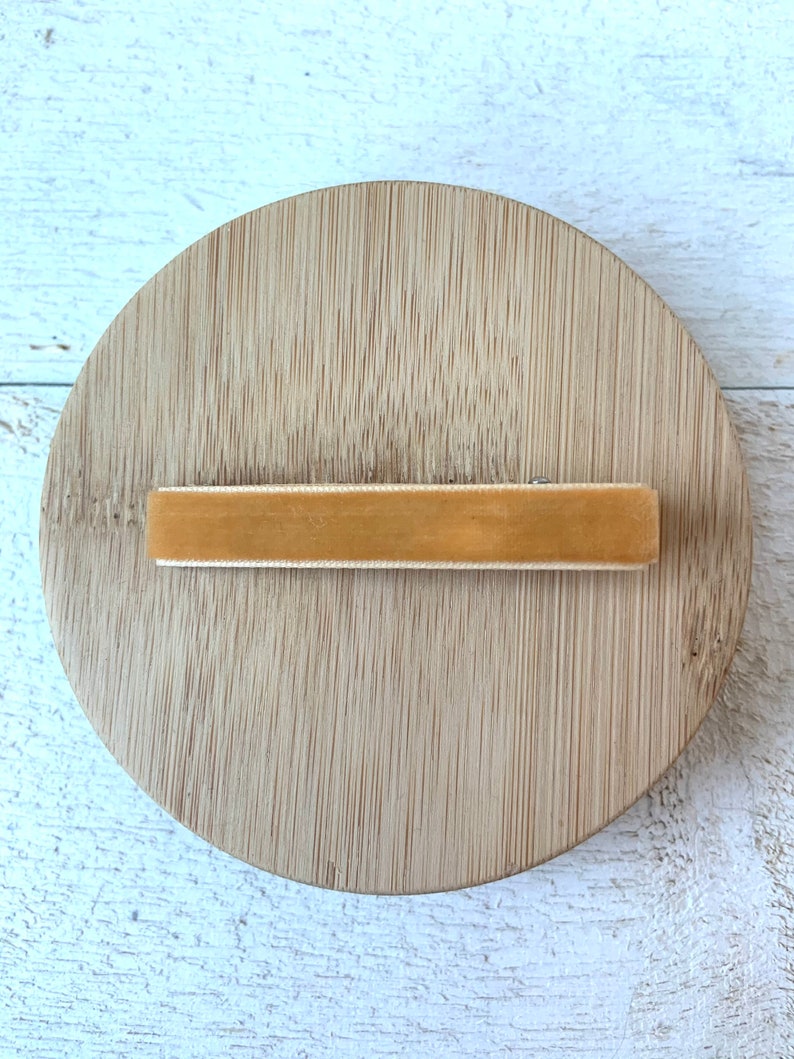 May include: A light brown velvet hair clip on a wooden surface.