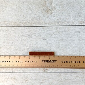 May include: A brown velvet ribbon measuring approximately 6 inches long, resting on a wooden ruler with the text "TODAY I WILL CREATE" and "FISKARS LIA GRIFFITH" printed on it.