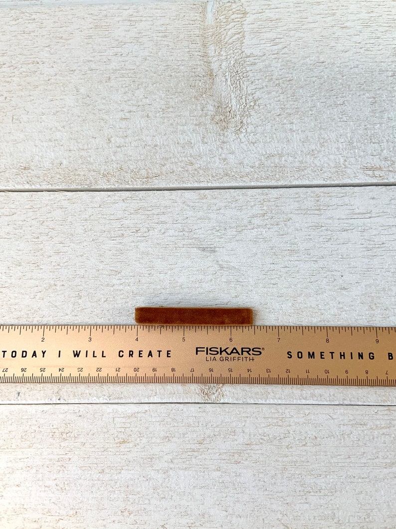 May include: A brown velvet ribbon measuring approximately 6 inches long, resting on a wooden ruler with the text "TODAY I WILL CREATE" and "FISKARS LIA GRIFFITH" printed on it.