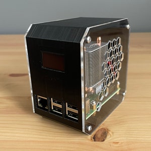 May include: A black computer case with a clear acrylic side panel, revealing a heatsink and fan. The case has a digital display and multiple USB ports.